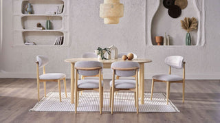 Dining room with a wooden table and chairs on a rug, against a neutral wall with shelves.