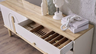 Wooden sideboard with open drawer containing cutlery, books, and decorative items.