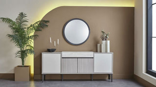 Modern interior with a sideboard, round mirror, and potted plants against a brown wall.