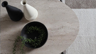 Decorative items including a black vase, white ceramic vase, and black bowl with greenery on a textured surface.