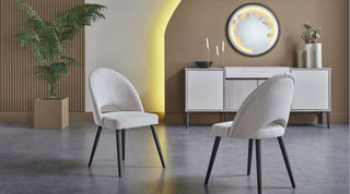 Two white chairs in a modern living room with a sideboard and decorative mirror.