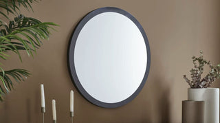 Round mirror with dark frame on a beige wall with decorative elements.