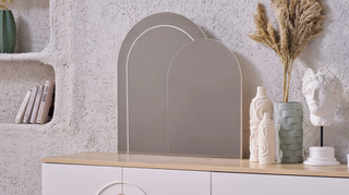 Decorative shelf with a mirror, books, and decorative items against a textured wall.